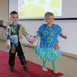 Chłopiec w kurtce z opakowań po przekąskach i czarnych spodniach z folii, pokazujący, jak zrobić strój ekologiczny dla chłopca.
