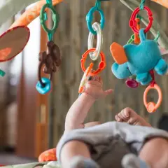 Niemowlę sięga do kolorowej zabawki sensorycznej dla niemowlaka, która wisi na łuku maty edukacyjnej.