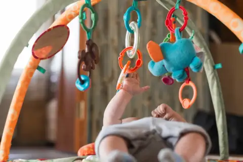 Niemowlę sięga do kolorowej zabawki sensorycznej dla niemowlaka, która wisi na łuku maty edukacyjnej.