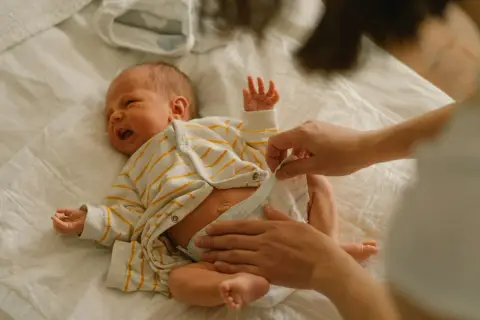 Mama zmienia pieluchę noworodkowi, zastanawiając się, jakie pieluchy dla noworodka będą najlepsze.