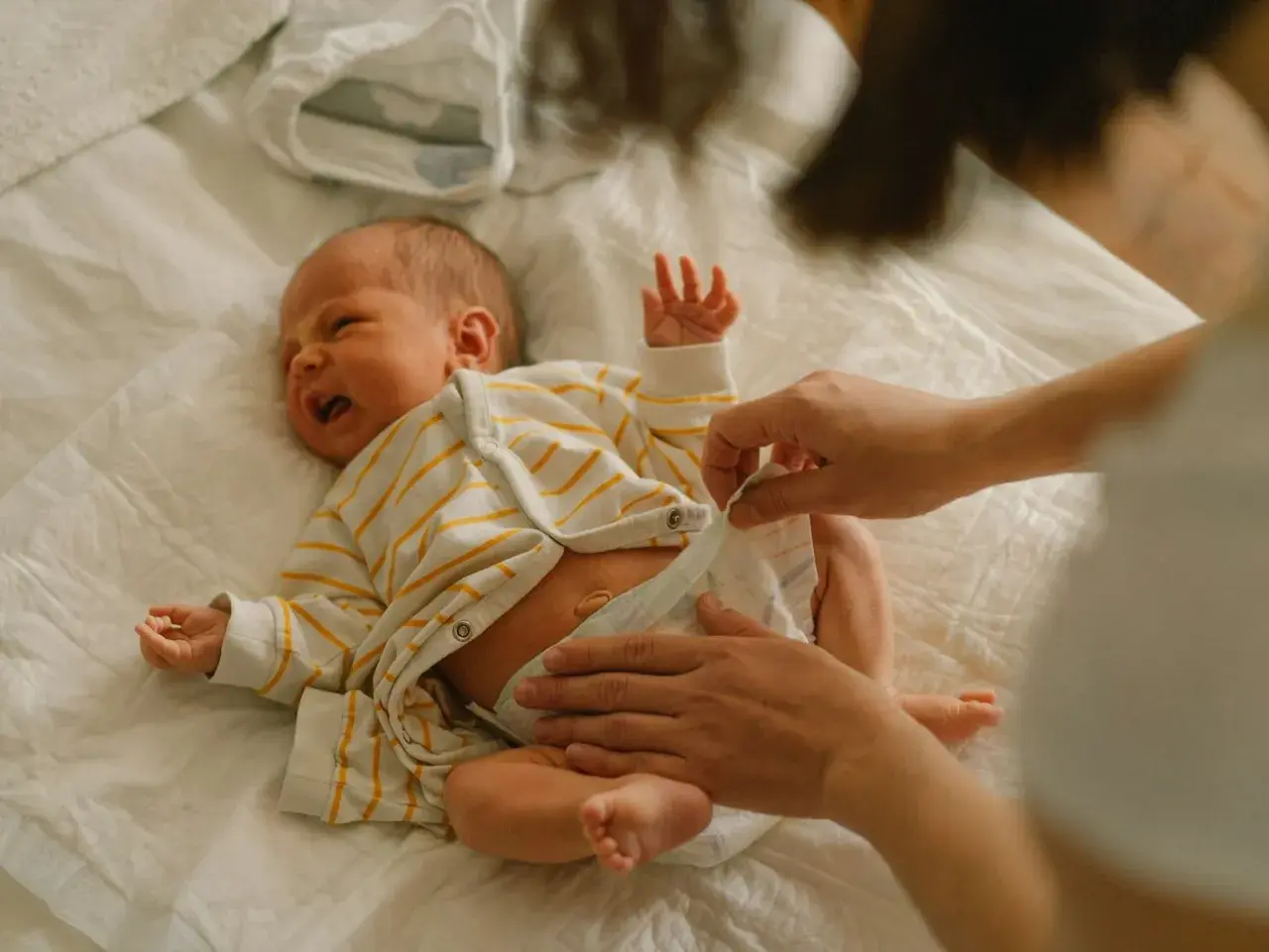 Mama zmienia pieluchę noworodkowi, zastanawiając się, jakie pieluchy dla noworodka będą najlepsze.